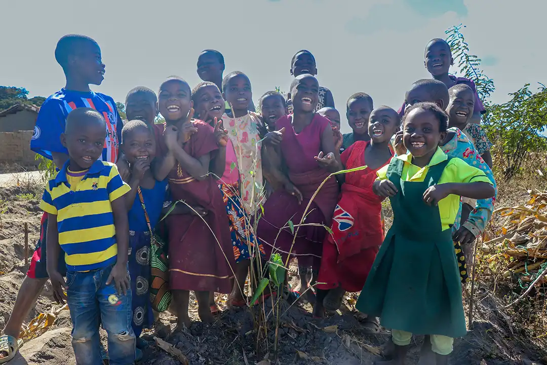 A group of African children all smile and laugh at the camera, they are stood closely together with their arms around eachother
